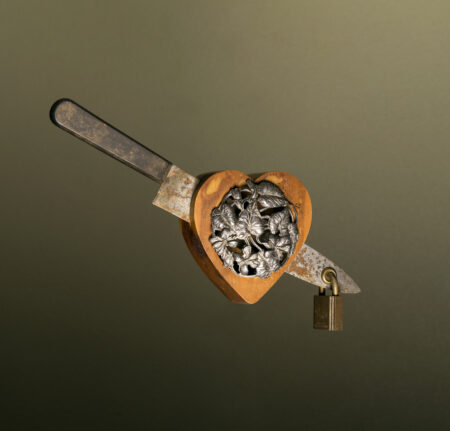 wooden heart with metal foliage on its face, with knife stuck through and padlock