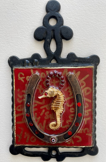 seahorse with red gem for eye, inside of a horseshoe with evil eye, writing and gold trim inside of iron frame