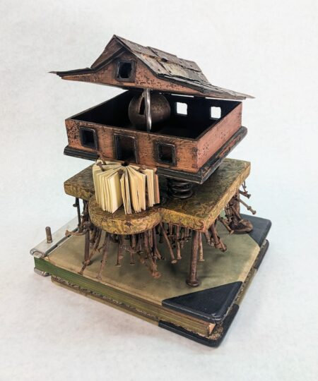 miniature house on a miniature table, held up by rusty nails, on top of vintage book
